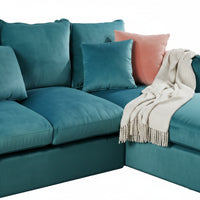 Teal sectional sofa with decorative pillows and a blanket on a white background