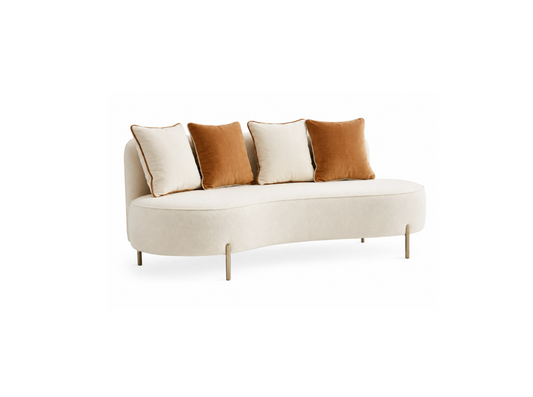 A curved upholstered daybed or chaise lounge in warm off-white fabric, styled with four throw pillows in cream and rust brown, supported by slim gold-toned metal legs, shown against a plain white background.
