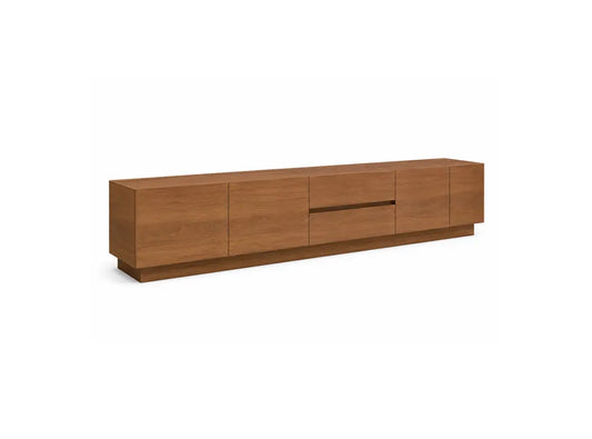 A modern long low media console with a warm medium-brown wood grain finish, featuring four cabinet doors and a central drawer with a recessed handle, shown on a plain white background.