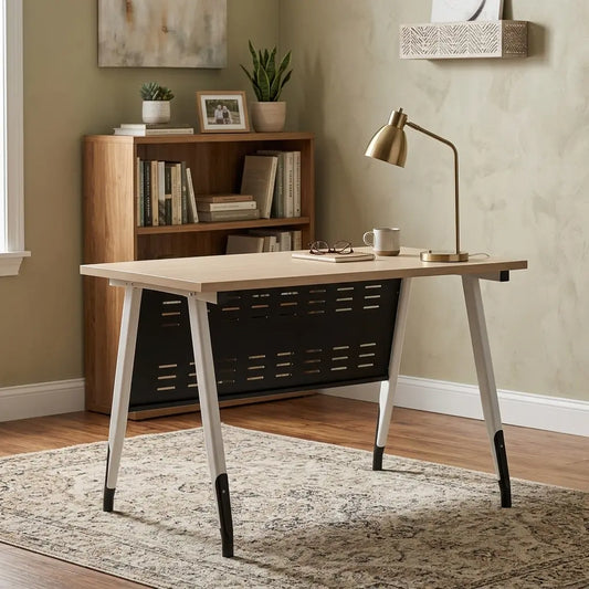A modern writing desk with a light wood top, black metal storage basket underneath, and white legs with black tips, styled in a home office setting next to a brass desk lamp.