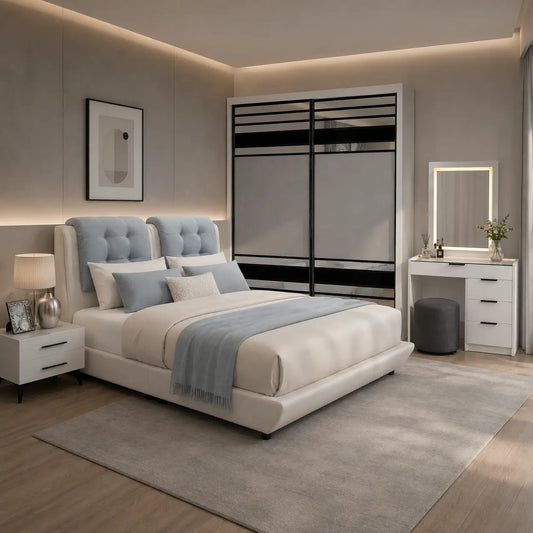 A modern bedroom featuring a light beige upholstered bed with a tufted light blue headboard, styled with white and blue bedding. The room includes a matching light gray rug, a white vanity table with a mirror, a white nightstand, and a large white sliding wardrobe with black accents.