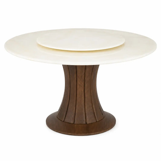 A round dining table featuring a cream-colored stone top with a matching inset plate, supported by a fluted dark brown wooden pedestal base.