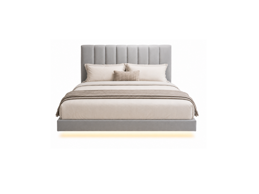 A modern platform bed with a tall, vertically channel-tufted headboard upholstered in light gray fabric, styled with neutral beige and white bedding, pillows, and a matching throw blanket. A warm glow of under-bed lighting is visible against a solid white background.