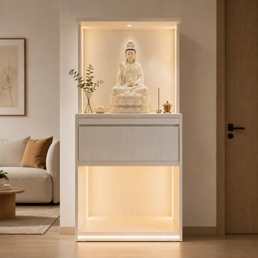 A modern white wooden altar cabinet with integrated warm LED lighting, featuring a white seated Buddha statue on top, shown in a minimalist living room setting.