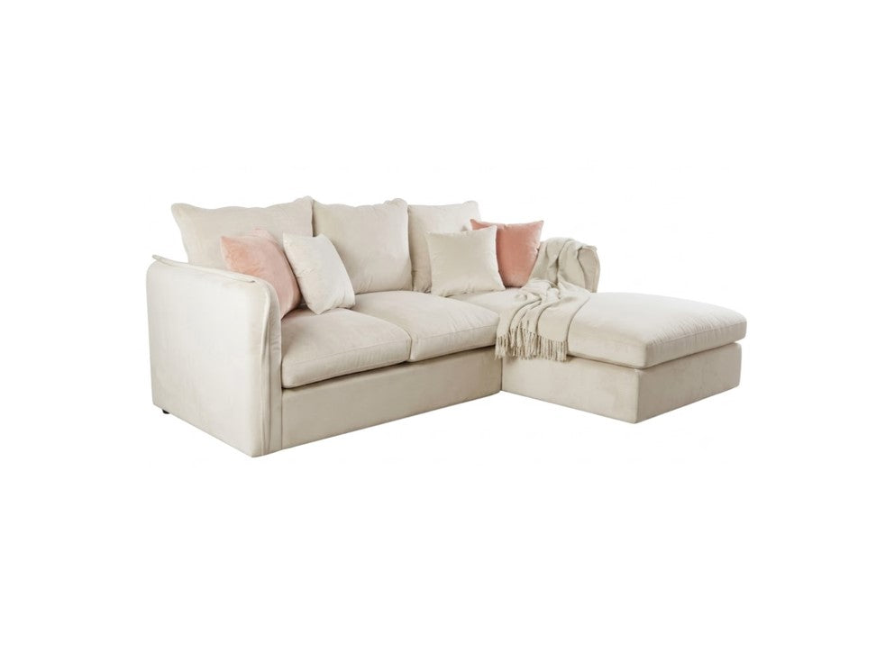 A cream-colored fabric sectional sofa with a chaise lounge on the right side, styled with several throw pillows in white and light pink, and a matching cream throw blanket draped over the armrest, set agains