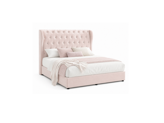 A light blush pink upholstered bed with a tall, button-tufted wingback headboard, styled with white bedding, pink accent pillows, and a matching pink throw blanket, set against a plain white background.
