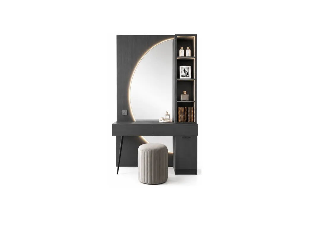 A modern vanity table set featuring a dark gray rectangular desk, a large arched mirror, built-in shelving on the right with decorative items, and a ribbed cylindrical ottoman in front, shown on a plain white background.