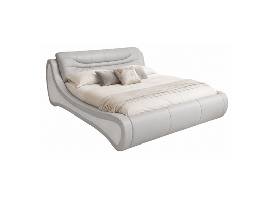 A modern low-profile platform bed with a curved, upholstered frame in light gray leather or faux leather, styled with cream and gray bedding and pillows, shown on a plain white background.