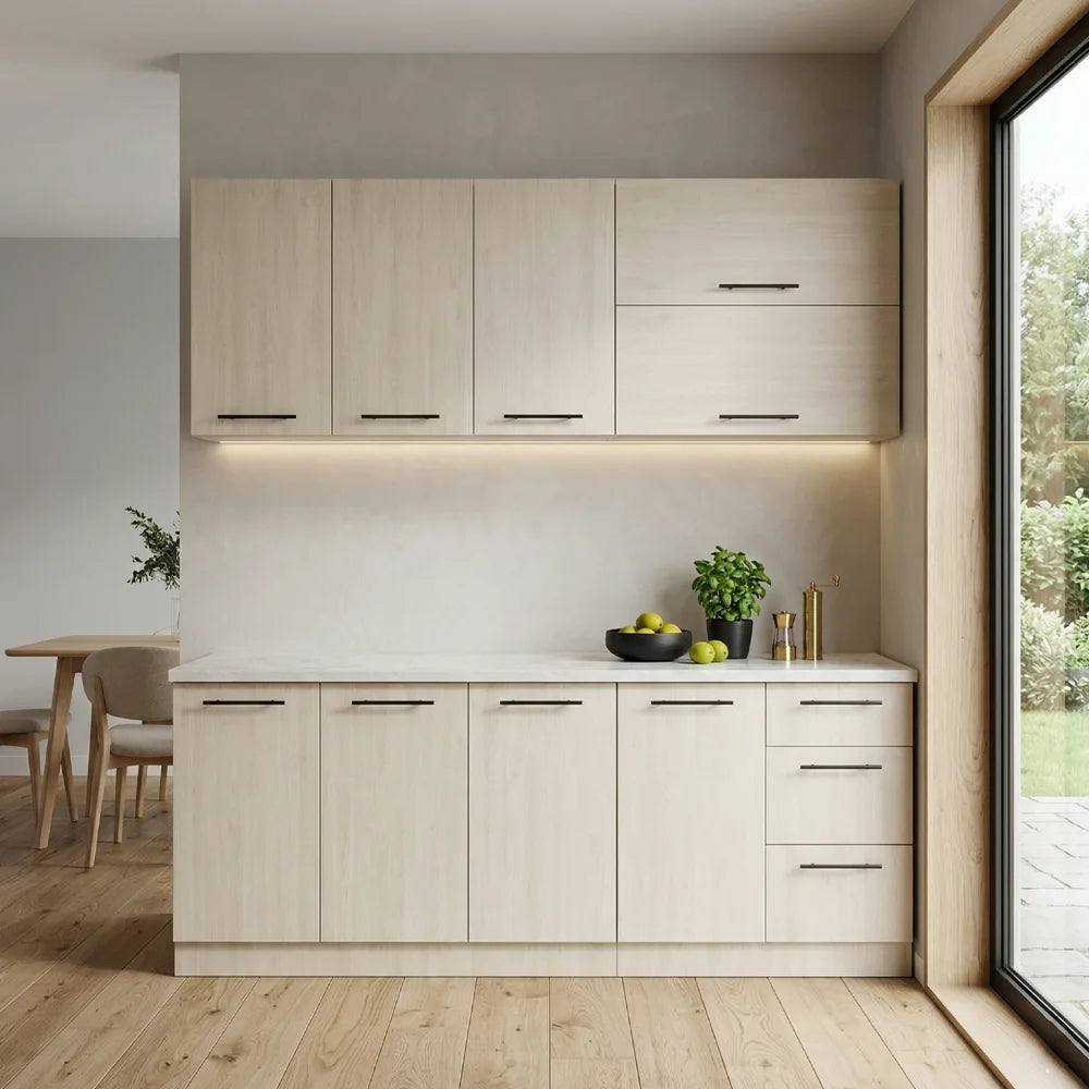A modern kitchen cabinet and drawer unit in a light wood grain finish, installed against a white wall beneath upper wall cabinets. The unit includes a white countertop with a small plant, fruit bowl, and gold-toned bottle holder.