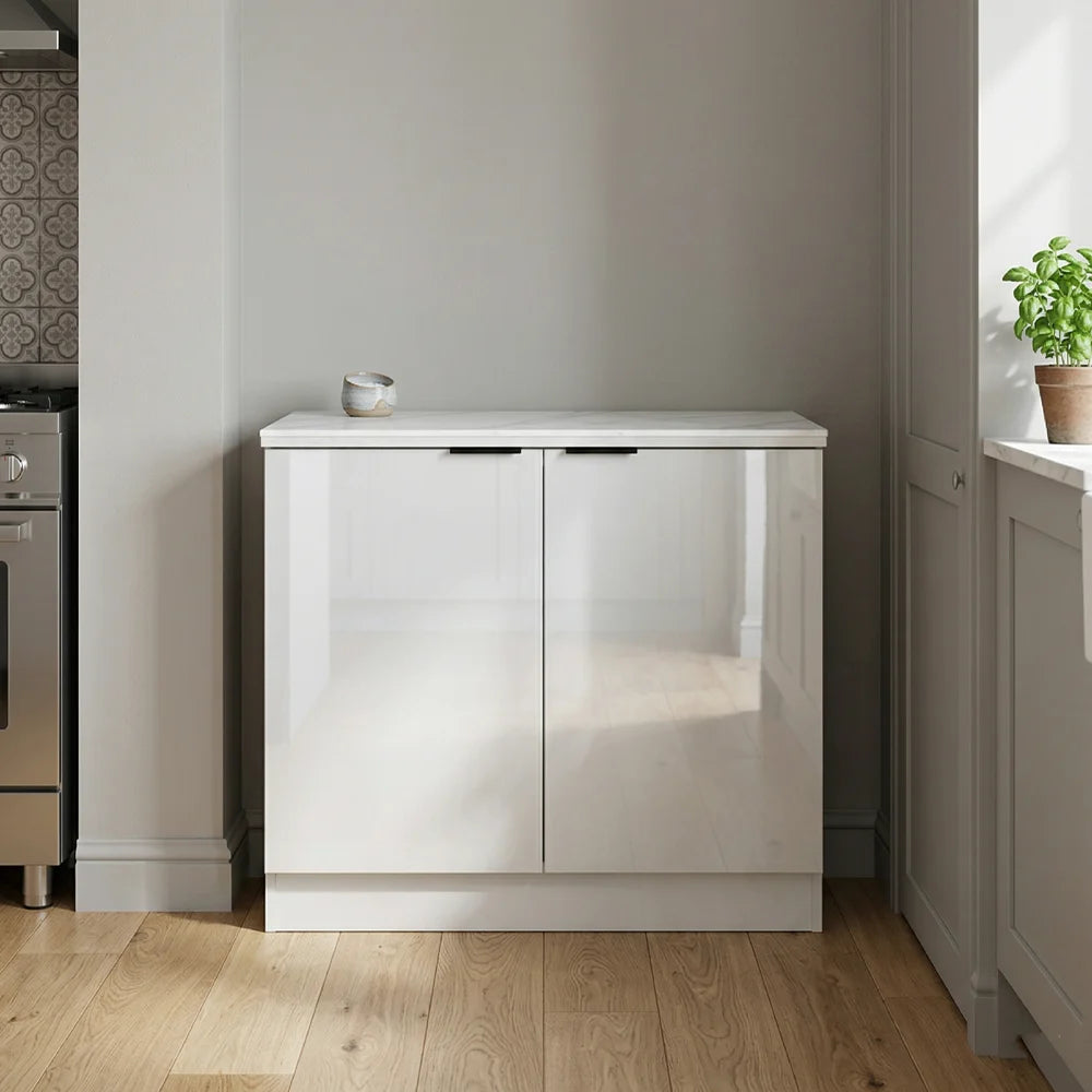 A modern white high-gloss two-door sideboard cabinet in a minimalist kitchen setting with light wood floors and neutral walls.