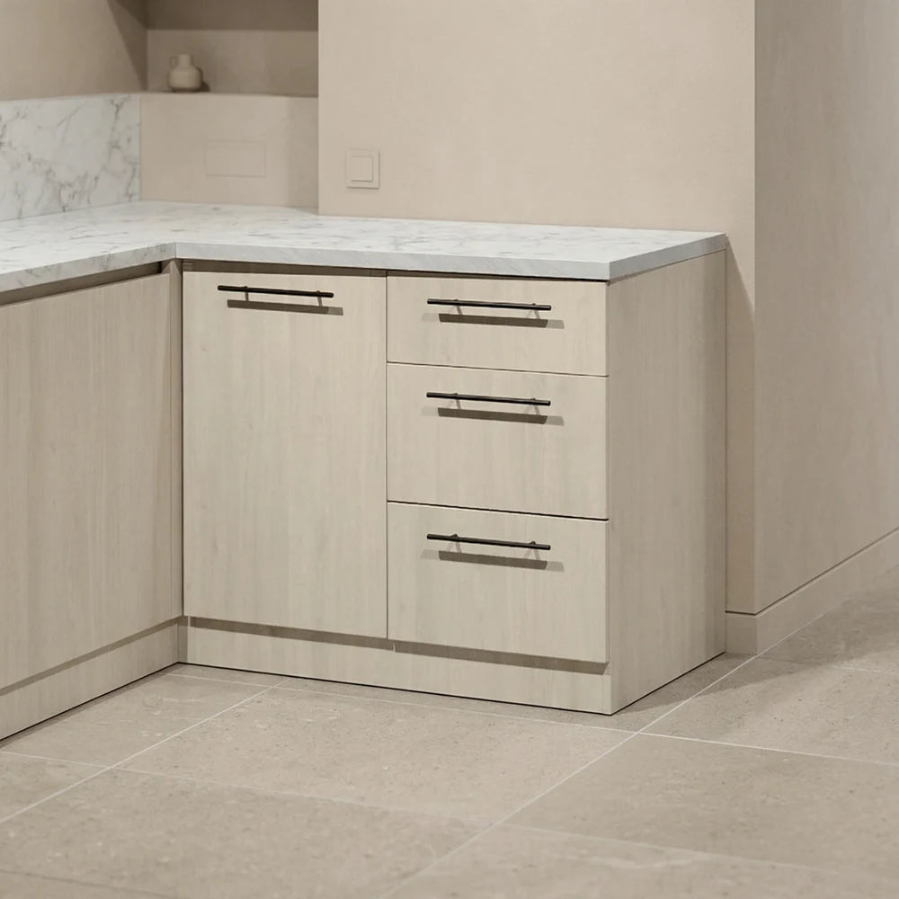 Light wood kitchen cabinetry with a white marble-look countertop and three drawers, shown in a modern kitchen setting with beige tile flooring.