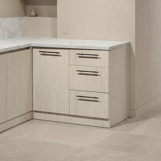 Light wood kitchen cabinetry with a white marble-look countertop and three drawers, shown in a modern kitchen setting with beige tile flooring.