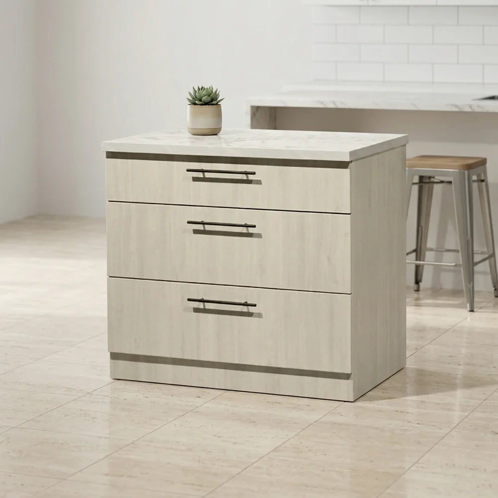 A three-drawer kitchen island cabinet with a light beige wood-grain finish and a white marble-look top, shown in a bright kitchen setting with a small potted succulent on top.
