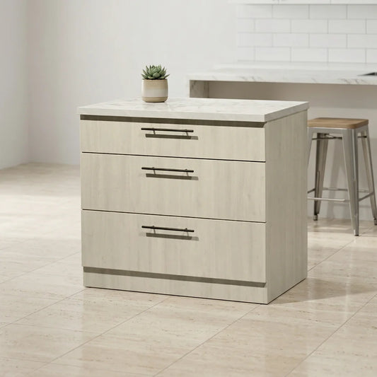 A three-drawer kitchen island cabinet with a light beige wood-grain finish and a white marble-look top, shown in a bright kitchen setting with a small potted succulent on top.