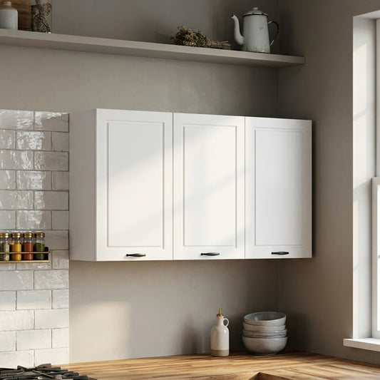 Three white shaker-style wall cabinets mounted on a beige wall in a modern kitchen setting, with a wooden countertop, white subway tile, and decorative items visible.