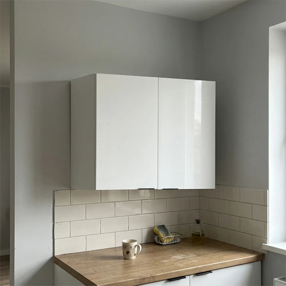 A pair of glossy white wall-mounted kitchen cabinets installed above a wooden countertop with a white subway tile backsplash